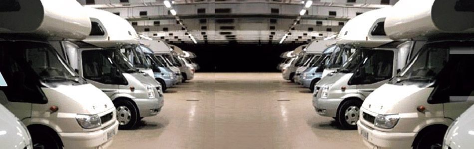 Filas de vehículos recreativos blancos estacionados dentro de un garaje o instalación de almacenamiento bien iluminado.