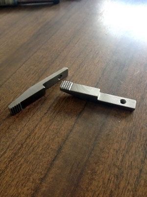 Dos pequeñas palancas de metal con extremos texturizados, colocadas sobre una superficie de madera.