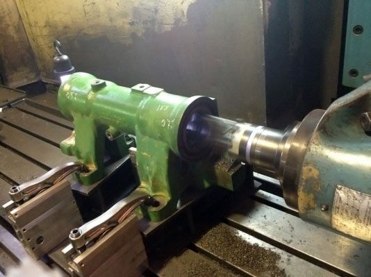 Pieza de máquina industrial verde fijada a una superficie metálica, probablemente para mecanizado.