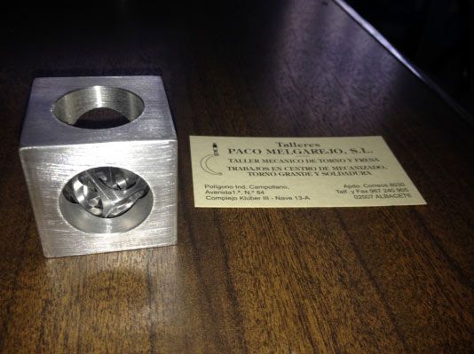 Cubo de metal con agujeros, junto a tarjeta de visita sobre madera.