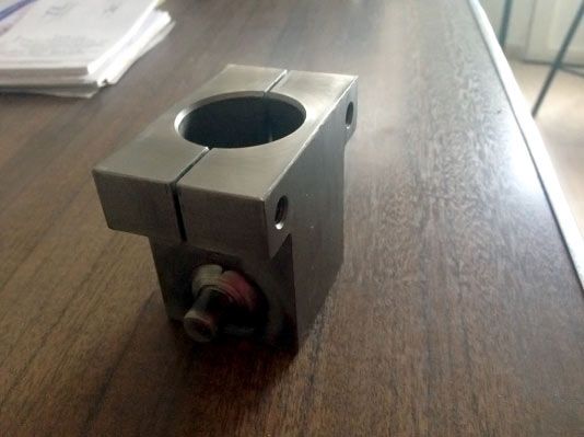 Dispositivo de sujeción metálico con apertura cilíndrica y perno, sobre superficie de madera.