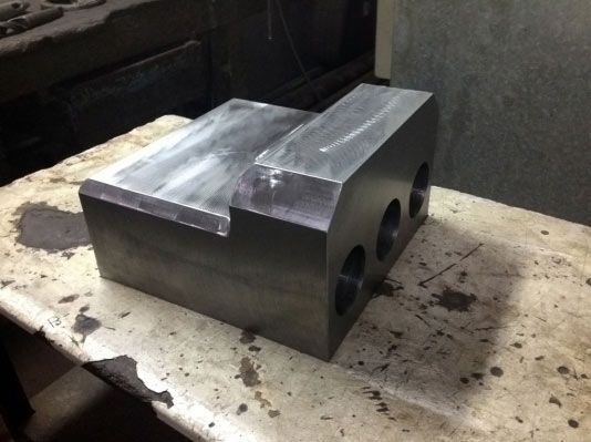 Un bloque de metal rectangular con tres agujeros perforados, colocado sobre una superficie de trabajo.