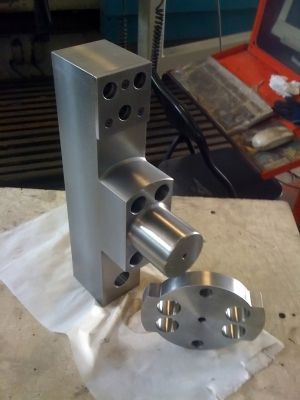 Conjunto de válvula hidráulica de metal mecanizado sobre banco de trabajo, con pieza circular separada.