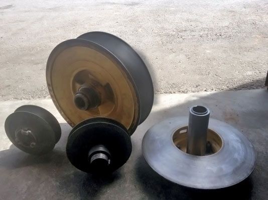 Cuatro poleas metálicas de diferentes tamaños, colocadas sobre una superficie de hormigón.