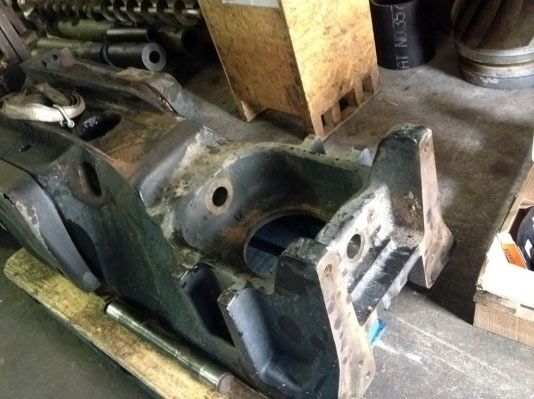 Un componente de máquina industrial grande y gris, con un orificio abierto y varios agujeros, en un entorno de taller.