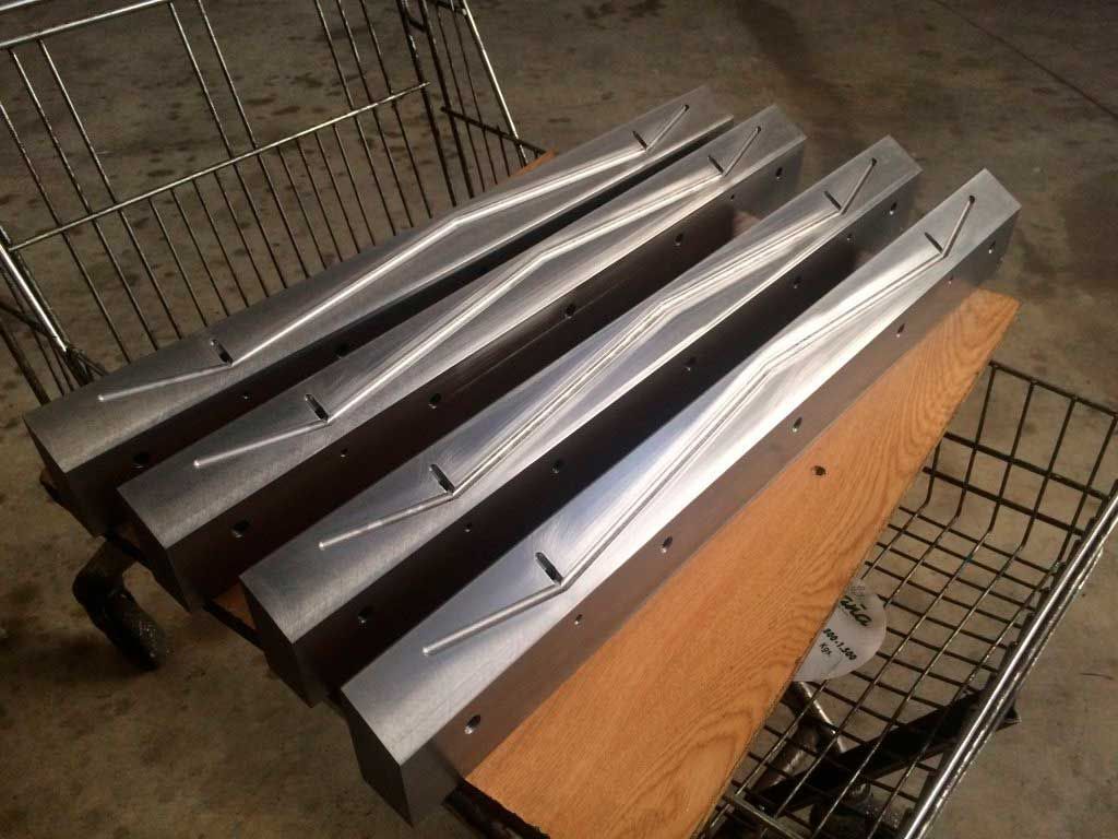 Cuatro formas metálicas angulares con canales tallados, apoyadas sobre madera, dentro de un carrito de compras.