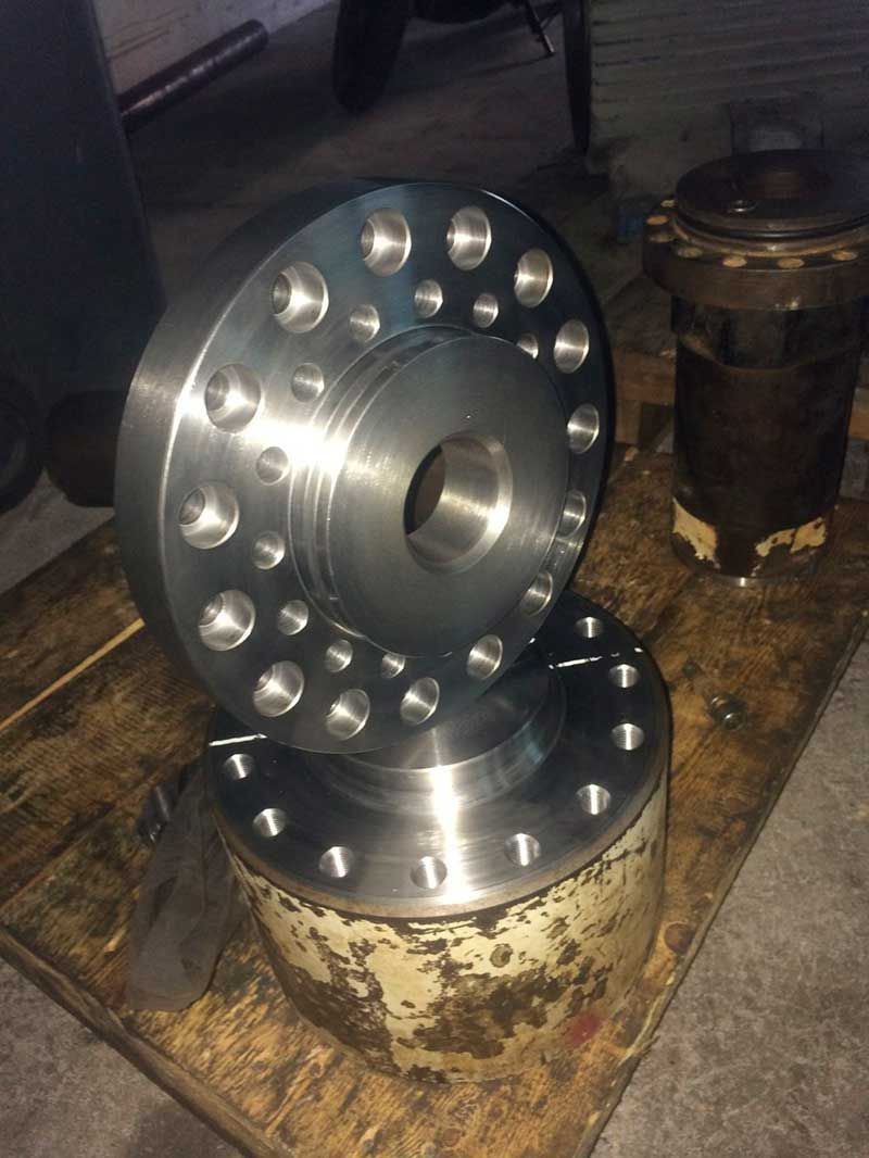 Dos bridas de metal brillante, una apilada sobre una base manchada de óxido, con múltiples agujeros perforados alrededor de sus perímetros.