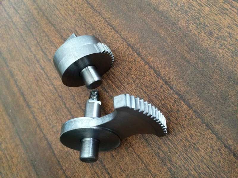 Dos piezas de una máquina de metal gris, una de ellas con un borde similar a un engranaje, yacen sobre una superficie de madera.