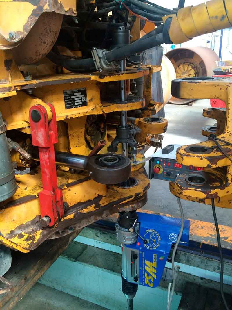 Herramienta industrial azul trabajando en una máquina pesada amarilla; al aire libre.