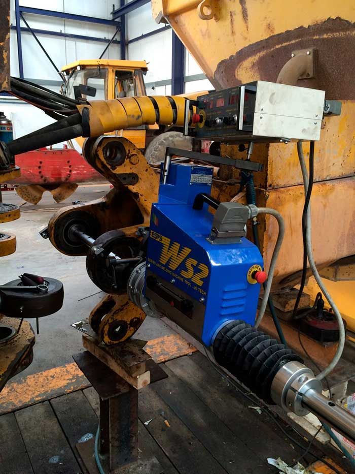 Máquina WS2 azul y negra unida a una pieza de excavadora amarilla en un taller.