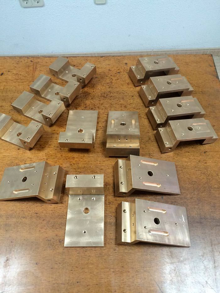 Múltiples piezas metálicas rectangulares de color latón dispuestas sobre una superficie de madera.