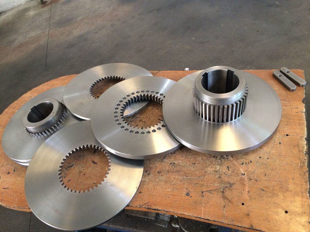 Cinco componentes de engranajes de metal sobre una superficie de madera; varios tamaños y diseños con características circulares y dentadas.