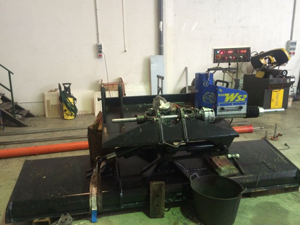 Una máquina quitanieves desmontada en un taller, con herramientas y equipos al fondo.