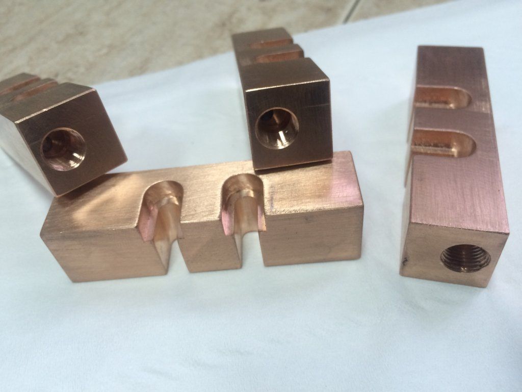 Componentes eléctricos de cobre con diversas características fresadas y orificios roscados.