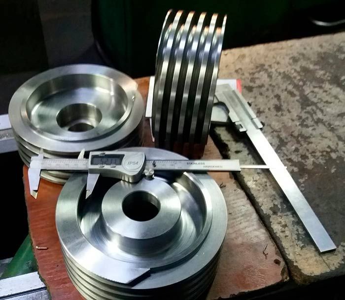 Tres poleas metálicas, una de ellas acanalada, con pinzas apoyadas sobre ellas, sobre un banco de trabajo.