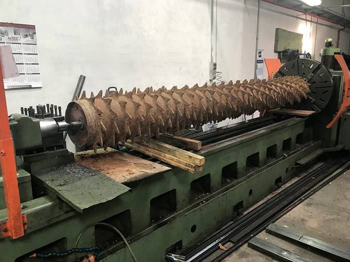 Una gran pieza de metal oxidado en un torno dentro de un entorno industrial.