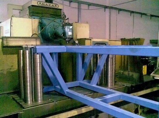 Gran máquina azul en un taller, con varios cilindros plateados, al lado de una máquina más grande.