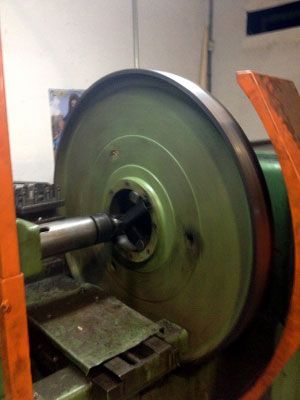 Rueda de torno grande de metal verde y negro en un taller. Protección naranja visible.