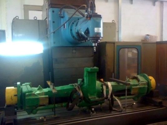 Eje de metal verde fijado a una fresadora para su reparación en un taller.