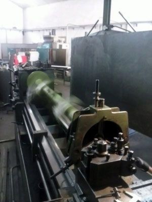 Un gran torno de metal mecanizando un objeto cilíndrico largo y verde en un taller.