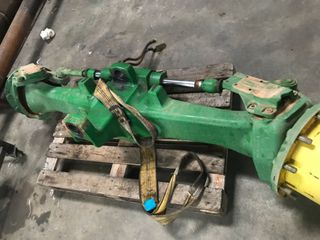 Eje de tractor John Deere verde sobre palet de madera, asegurado con una correa.