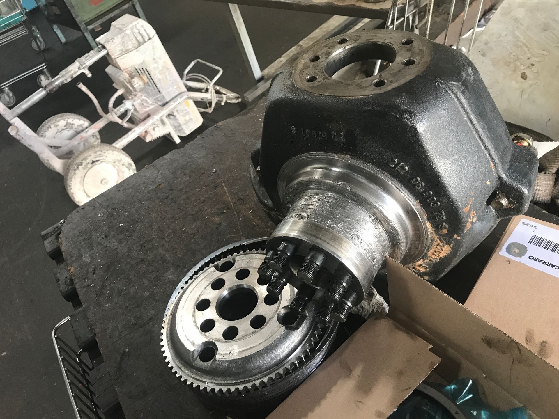 Componente de maquinaria negro desmontado con un engranaje circular visible, sobre un banco de trabajo.