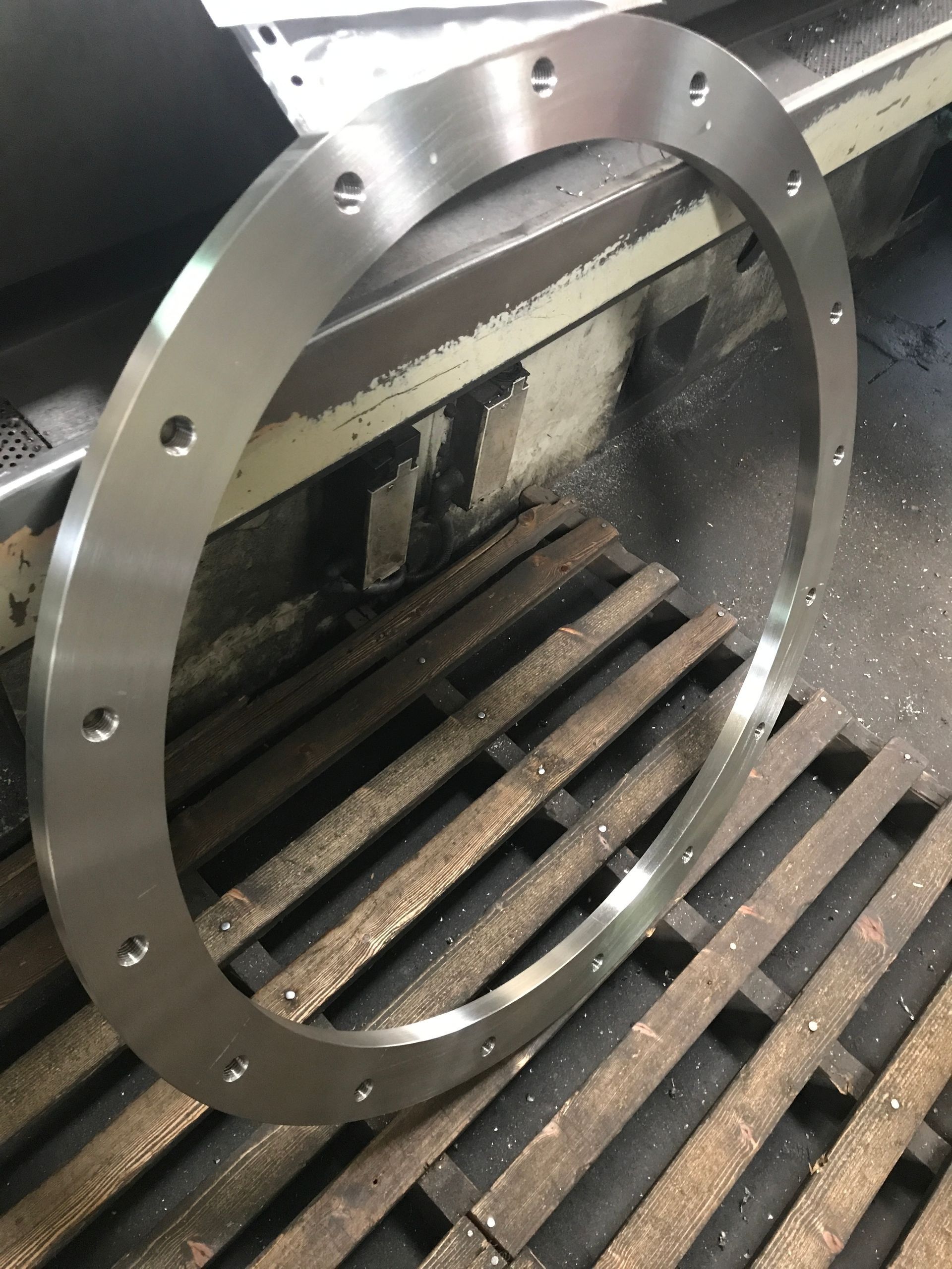 Anillo de metal con orificios para pernos espaciados uniformemente, apoyado sobre una rejilla de metal, probablemente en un entorno industrial.