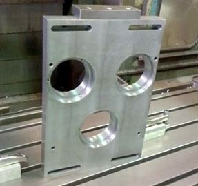 Placa de metal mecanizada con tres agujeros grandes y agujeros de montaje ranurados en una fresadora.