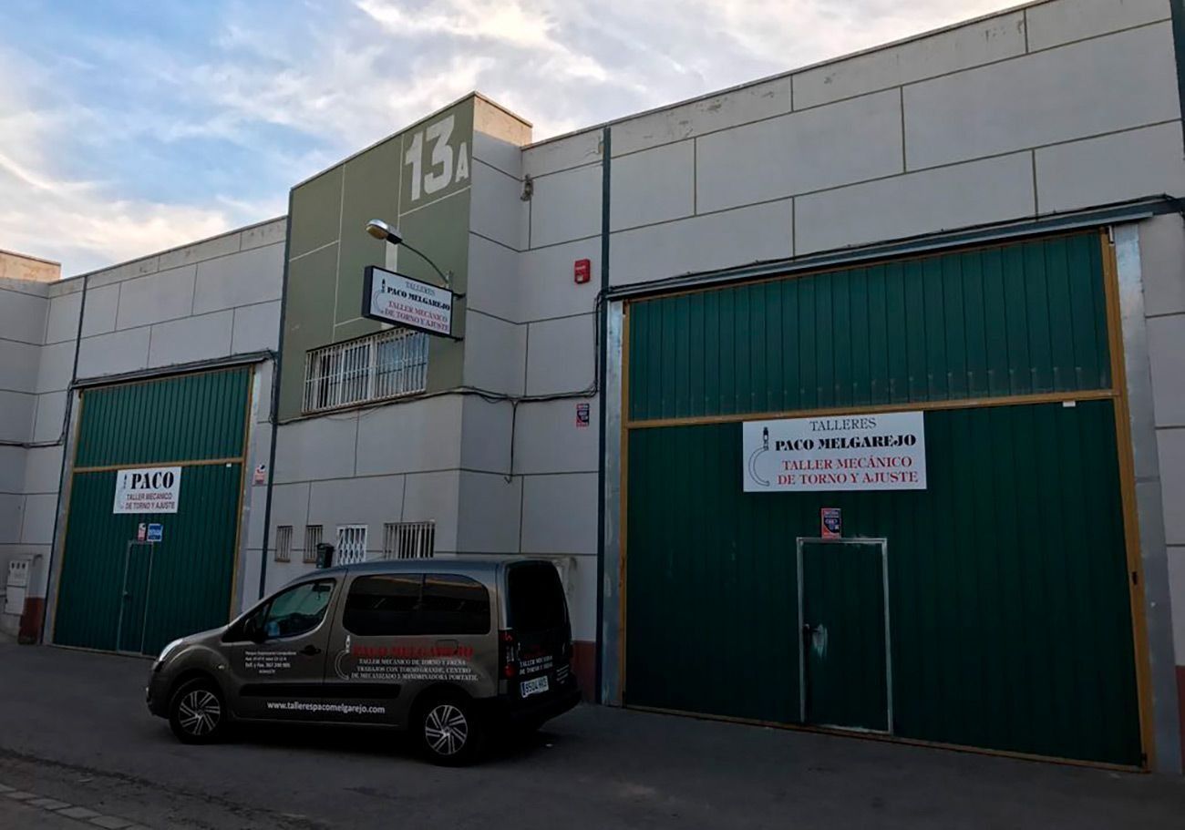Exterior de un almacén con puerta verde y señalización. Hay una furgoneta estacionada enfrente.
