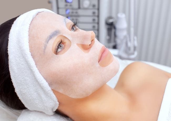 Una mujer está acostada en una cama con una máscara blanca en la cara.