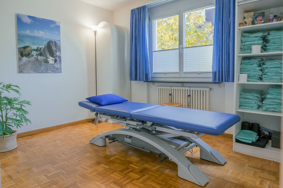 Physio-Parkallee GmbH - Therapieraum der Praxis mit blauer Physiotherapieliege, Bild an Wand, Regal mit Handtüchern