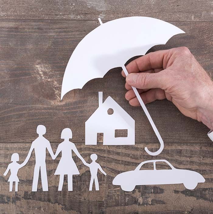 Una persona sostiene un paraguas sobre un recorte de papel de una casa, un automóvil y una familia.