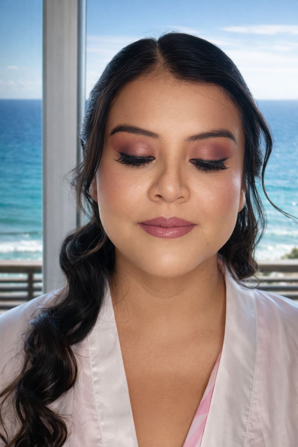 Mujer con los ojos cerrados, con sombra de ojos rosa, junto a una vista al mar.