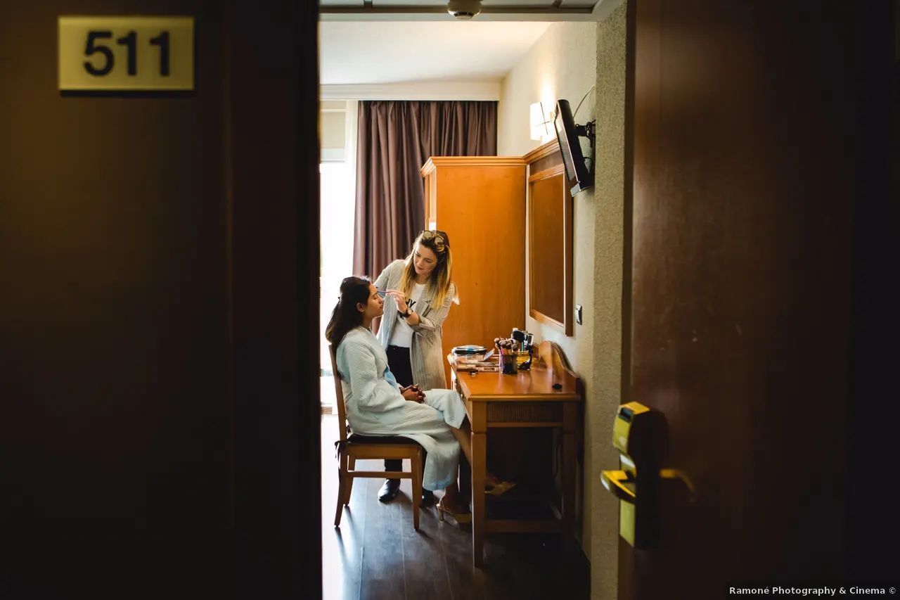 A una mujer le aplican maquillaje en la habitación del hotel, con la puerta abierta.