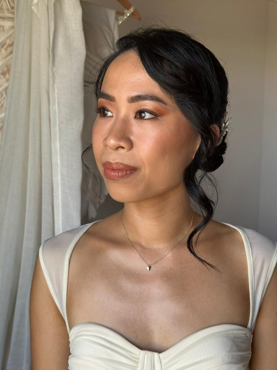 Mujer con cabello oscuro peinado hacia arriba, con un vestido blanco. Maquillaje: sombra de ojos naranja y lápiz labial 