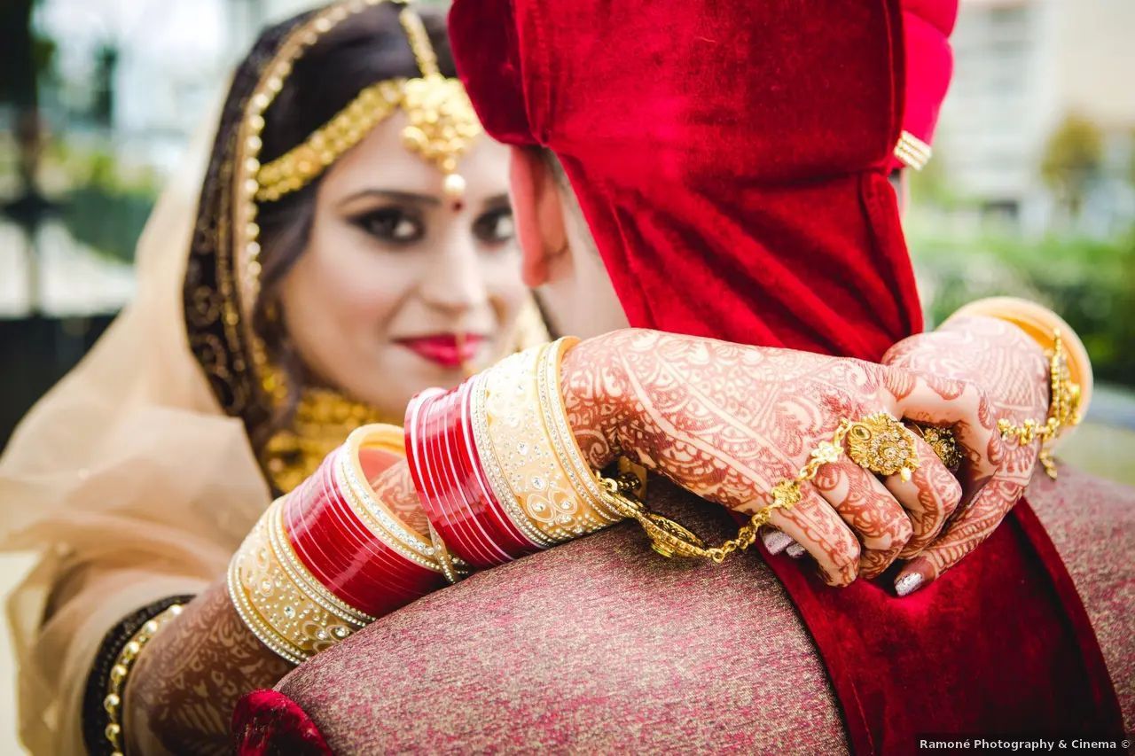La novia con velo dorado abraza al novio, con los brazos alrededor de su velo rojo.