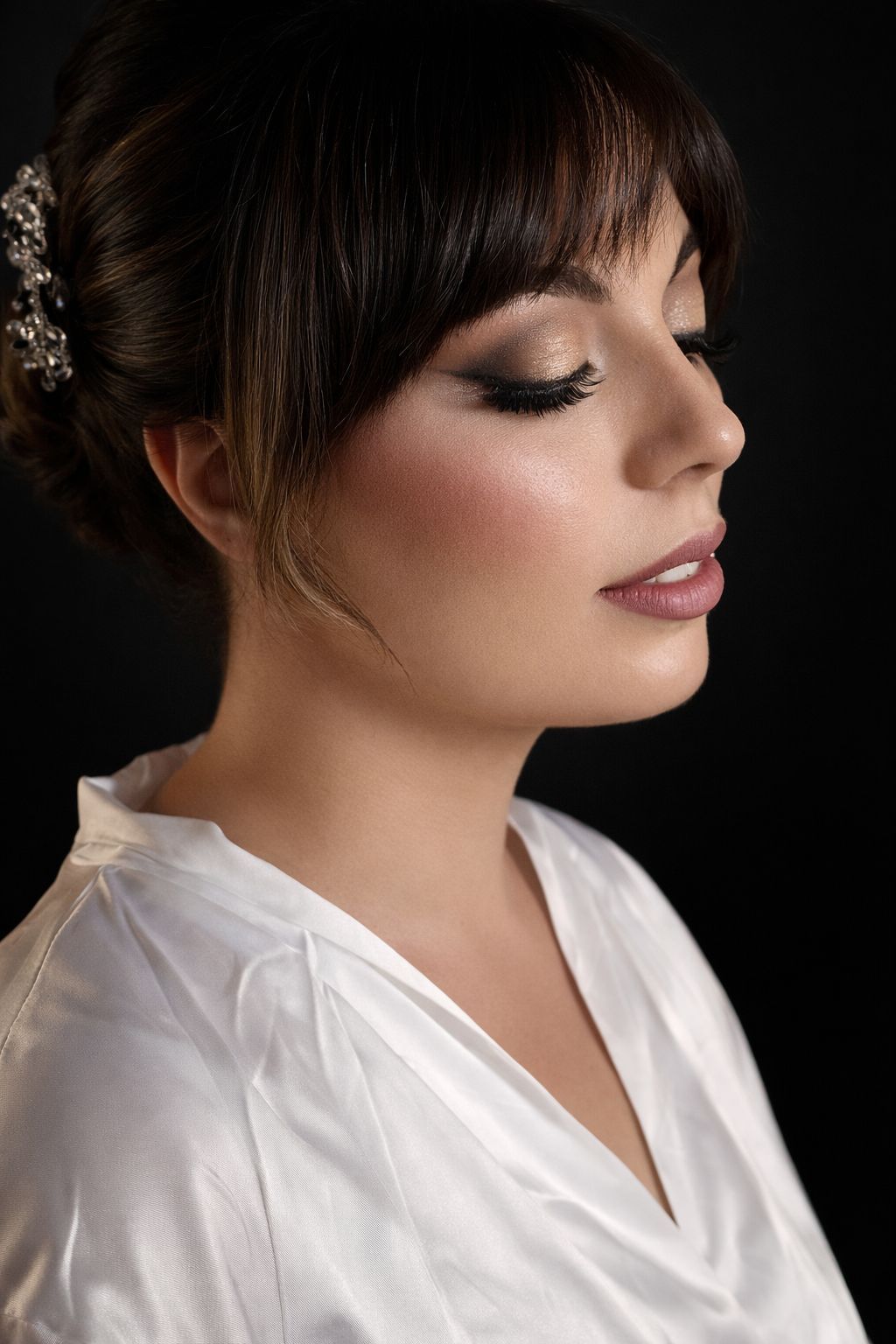 Mujer con un elegante recogido, maquillada y con una bata blanca sobre un fondo negro.
