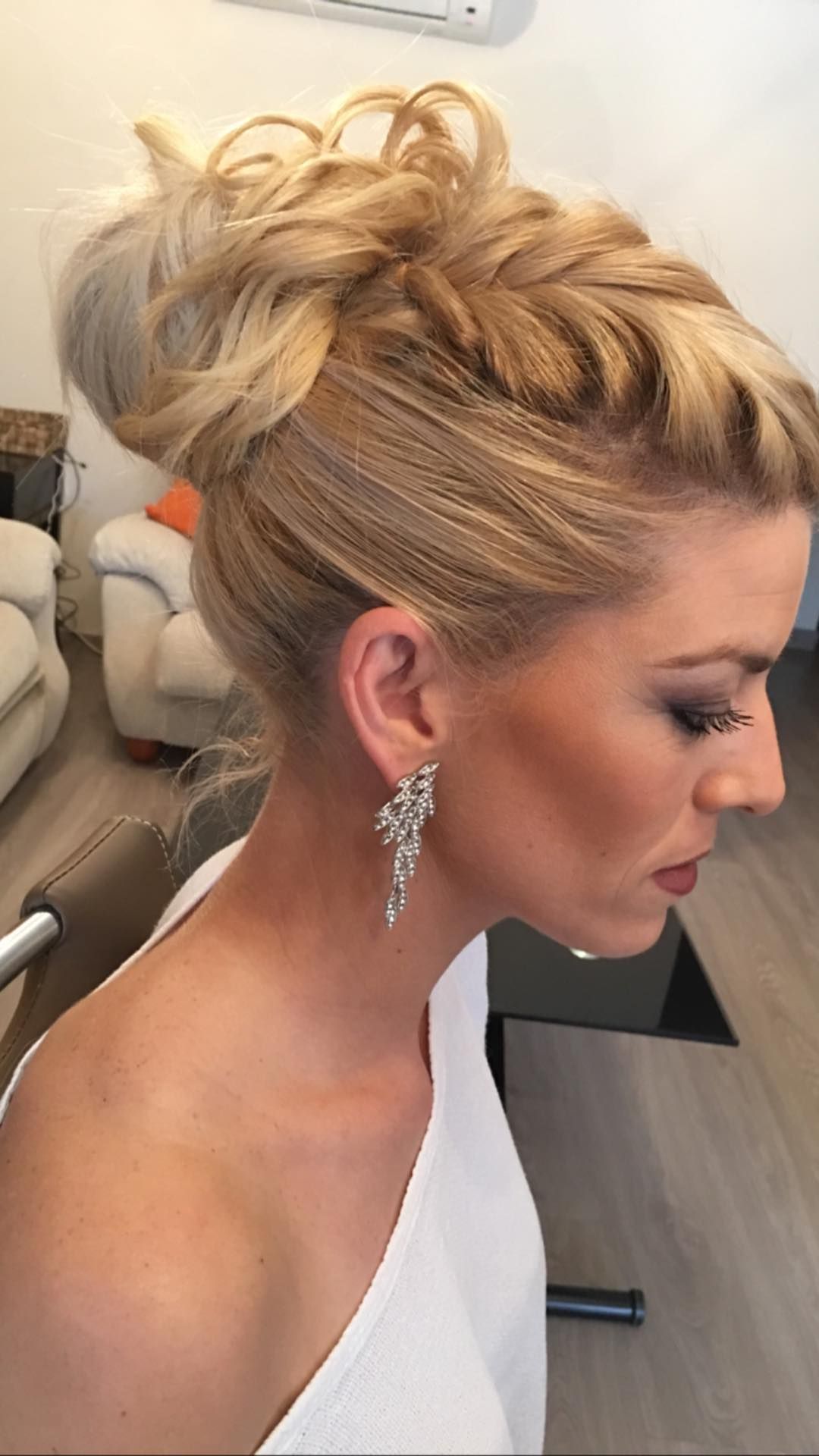 Mujer con recogido rubio, con top blanco y pendientes colgantes, mirando hacia abajo.