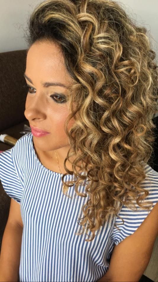 Mujer con cabello rizado y maquillaje, vistiendo un top de rayas azules y blancas, mirando hacia un lado.