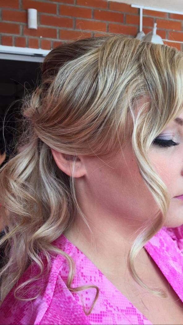 Mujer con cabello rubio ondulado, vestida con una túnica rosa, perfil lateral con maquillaje de ojos.