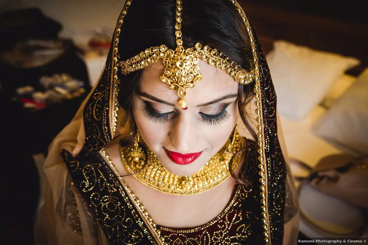 Mujer con joyas de oro y cubierta la cabeza, mirando hacia abajo, lápiz labial rojo.