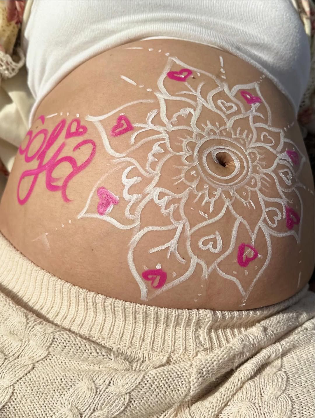Vientre de embarazada decorado con un diseño floral blanco, corazones rosas y el nombre 