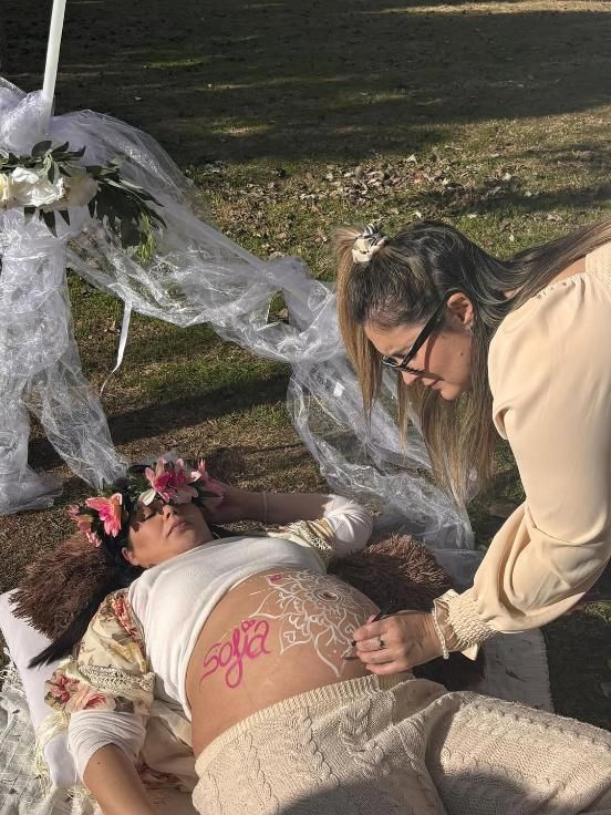 Persona embarazada con corona floral con diseño de henna en el vientre, al aire libre.