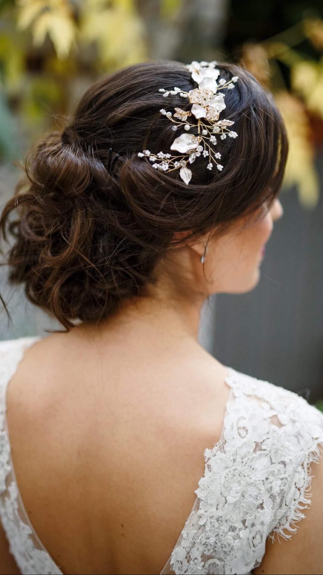 Mujer con cabello oscuro recogido, luciendo un tocado floral y luciendo un vestido de novia de encaje blanco.