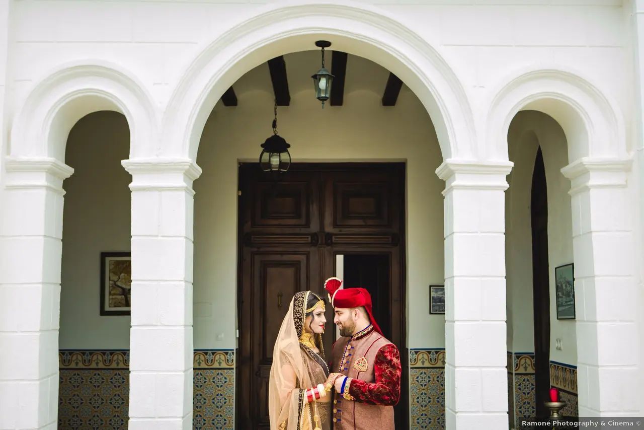 Una pareja con el traje de boda tradicional se miran el uno al otro debajo de una puerta arqueada.