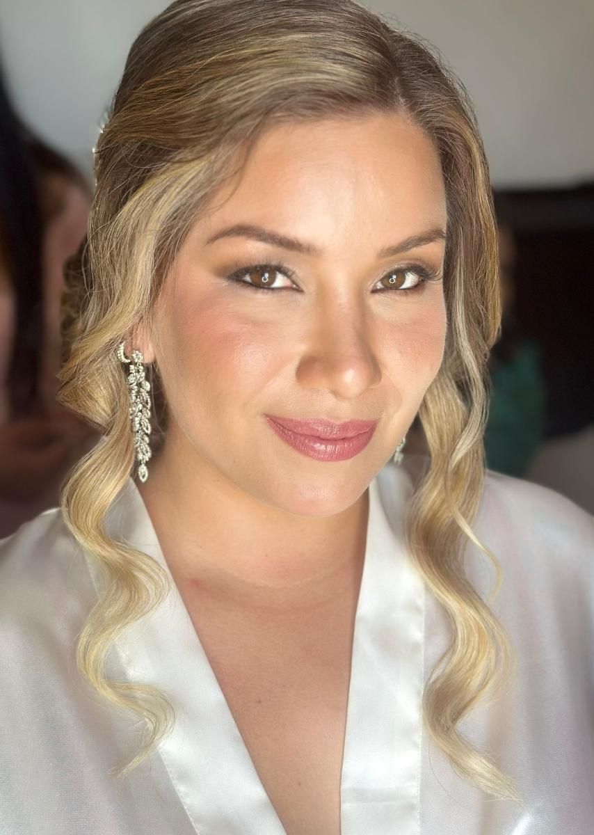 Mujer de cabello rubio ondulado, vestida con túnica blanca y pendientes, con maquillaje de boda.