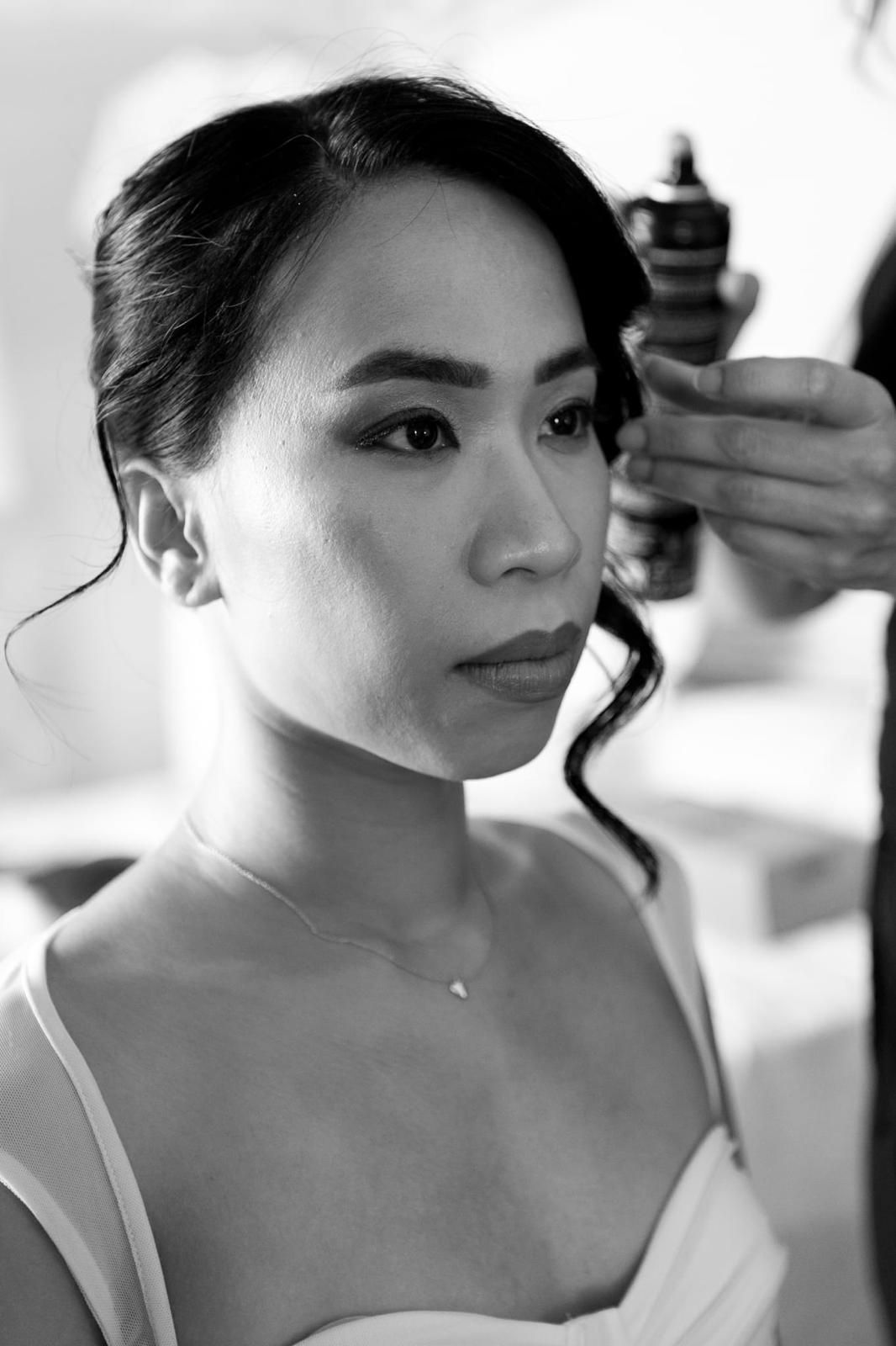 Mujer con peinado recogido, recibiendo laca para el cabello durante la preparación; iluminación suave.