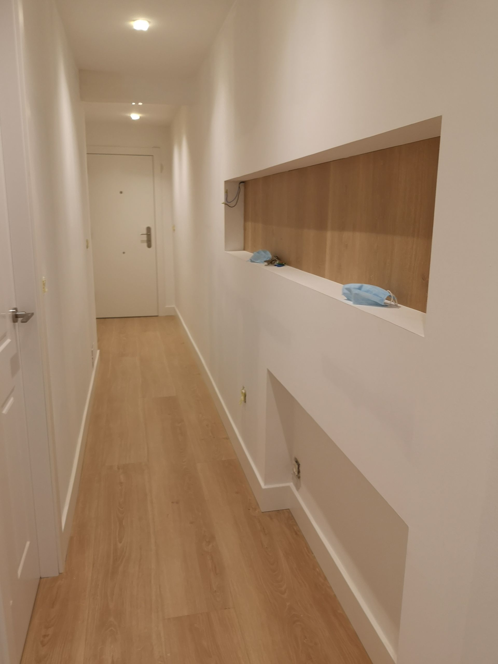 Un largo pasillo con suelos de madera y paredes blancas.
