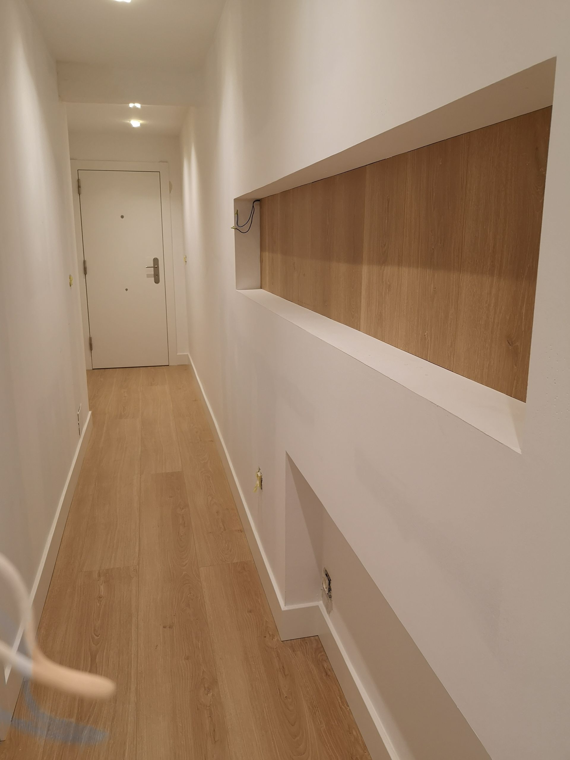 Un largo pasillo con suelos de madera y paredes blancas.