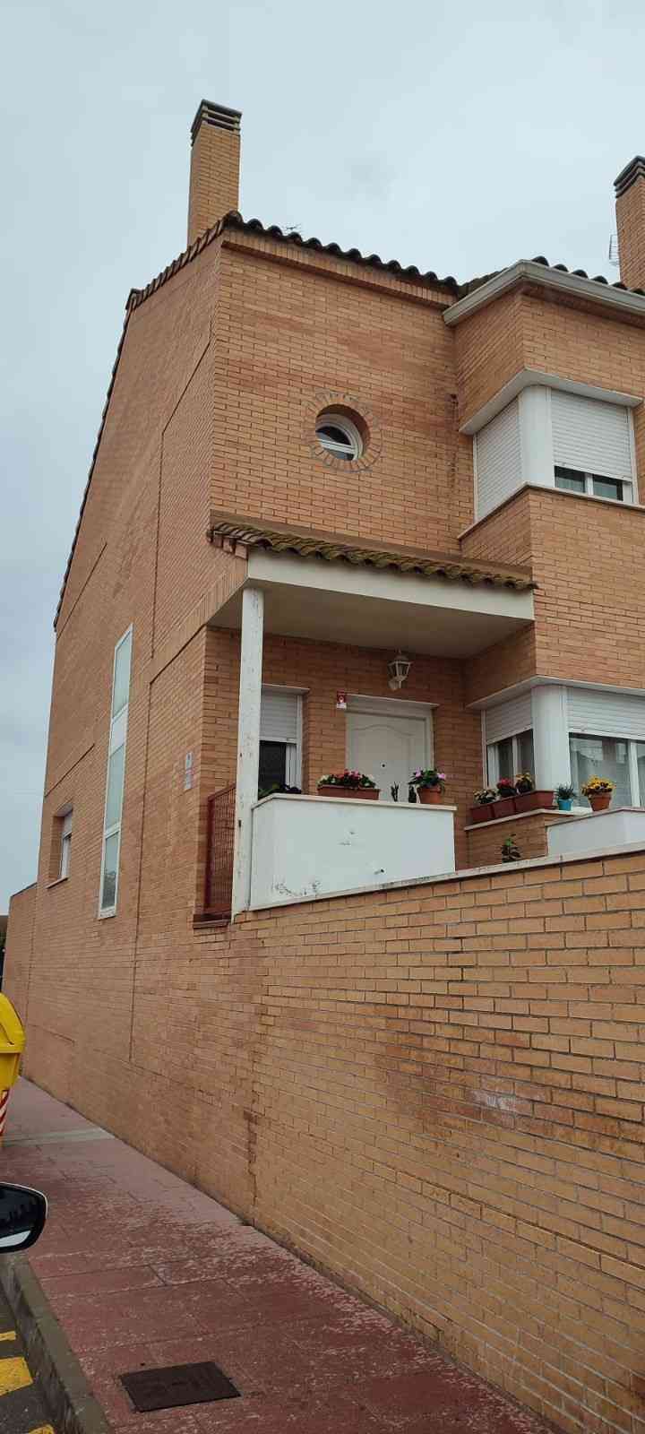 Edificio de ladrillo con pequeño balcón y chimenea bajo un cielo nublado.